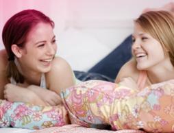Kuva kahdesta nuoresta tytöstä sängyllä nauramassa. Kuva kuvastaa murrosiän aiheuttamia monia muutoksia vartalossa, ja kuinka se on täysin normaalia.